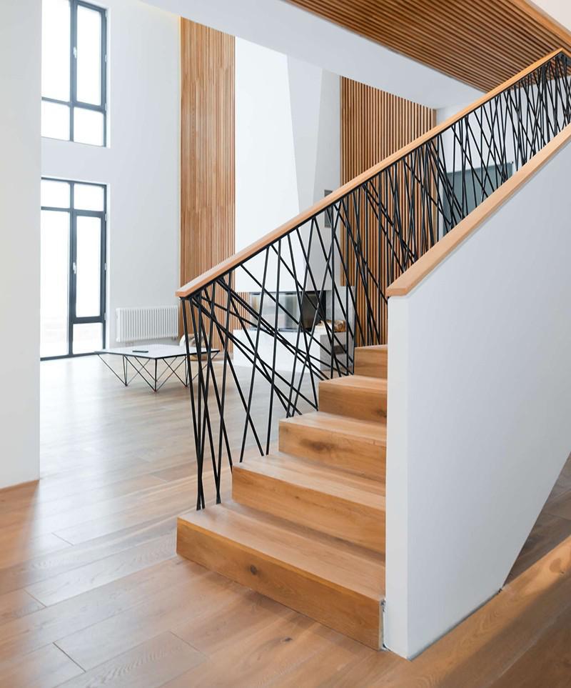 Escaleras de madera con pared blanco y una reja negro con líneas curvas.